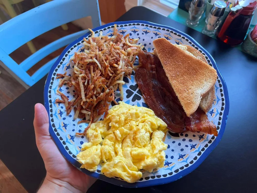 Scrambled eggs, bacon, toast and hash browns on a blue patterned plate